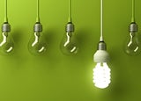 5 lightbulbs hanging in front of green background, one is lit up