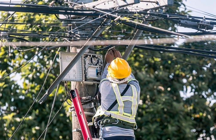 A technician on a ladder fixes a pole mounted fiber optic terminal splitter box to repair or restore internet connection to nearby houses.