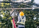 A technician on a ladder fixes a pole mounted fiber optic terminal splitter box to repair or restore internet connection to nearby houses.