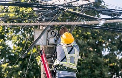 A technician on a ladder fixes a pole mounted fiber optic terminal splitter box to repair or restore internet connection to nearby houses.