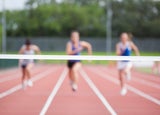 3 runners in soft focus on a track running towards the finish line