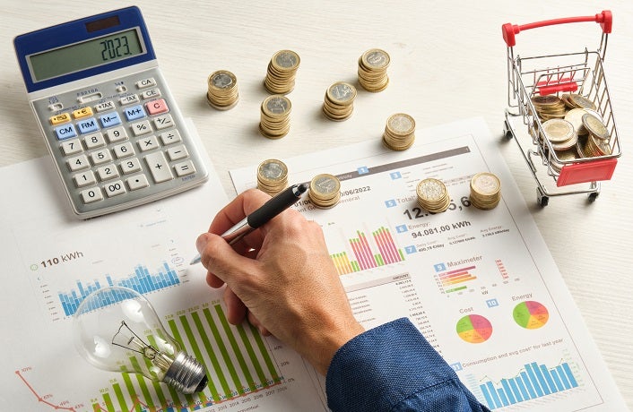 hand of a man with a pen on some electricity bills surrounded by coins a light bulb and a calculator