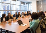 a group of people sat around a workplace meeting table in discussion