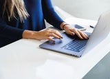 Woman's hands typing on a laptop on a white desk