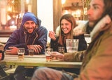 Happy friends drinking beers at trendy chalet pub restaurant in mountains on evening time - Young people having fun in winter vacation - Friendship and youth concept - Soft focus on woman face