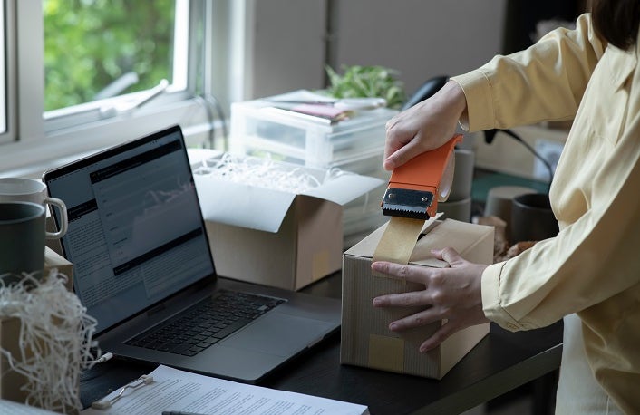 Closeup view of female online store small business owner seller entrepreneur packing package post shipping box preparing delivery parcel on table. Ecommerce dropshipping shipment service concept.