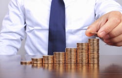 Mid shot of a businessman's torso in front of a table adding to piles of coins