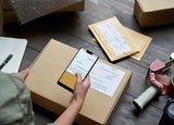 Female warehouse worker scanning barcode on shipping box on smartphone.