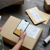 Female warehouse worker scanning barcode on shipping box on smartphone.