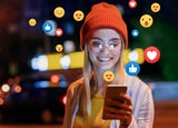 Woman smiling and looking at phone with emojis all around her