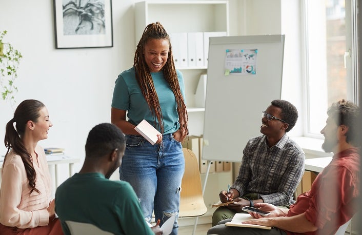 Multi-ethnic group of people sitting in circle while discussing business project in office, focus on smiling African-American woman talking to colleagues, copy space