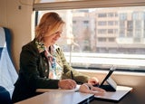 Woman works from a train with a tablet and a notebook. Working remotely, travel